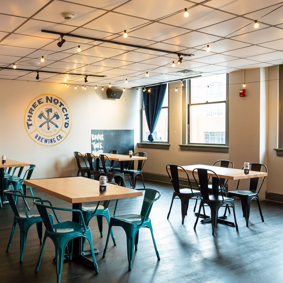 A bright dining room with teal chairs and the Three Notch'd badge on the wall